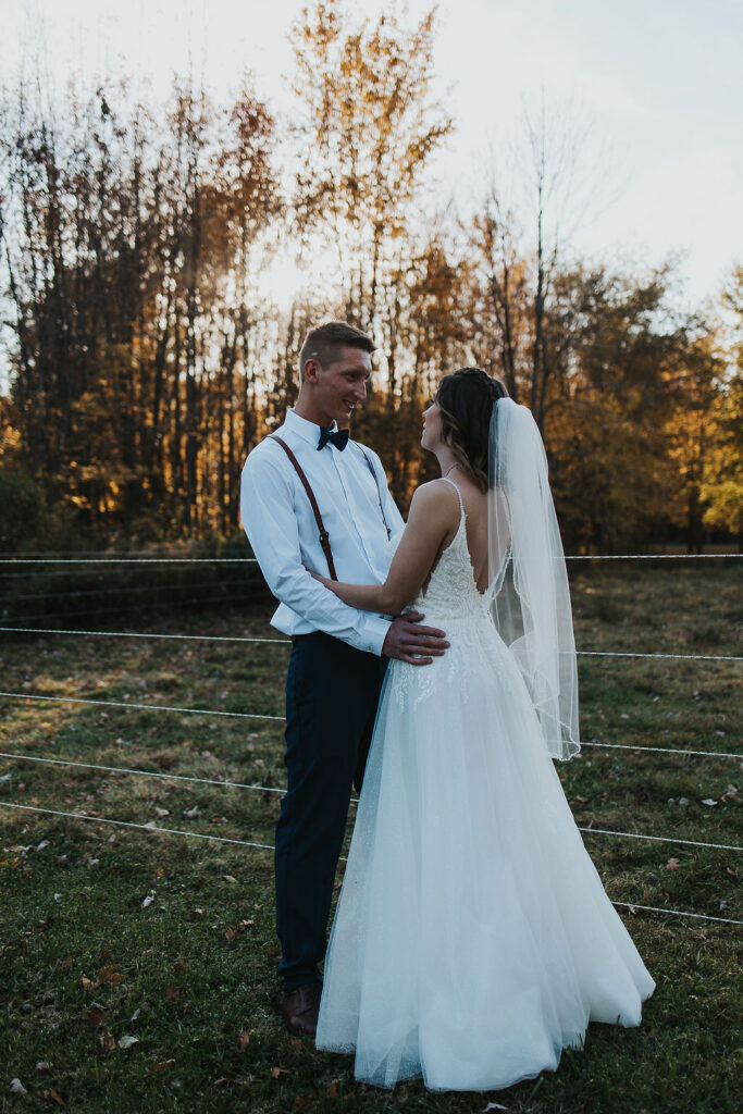 couple embrace along fence in pasture
