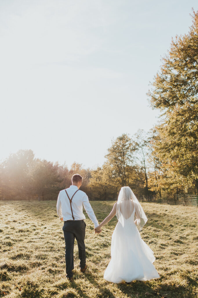couple walks holding hands in the pasture after their intimate backyard wedding