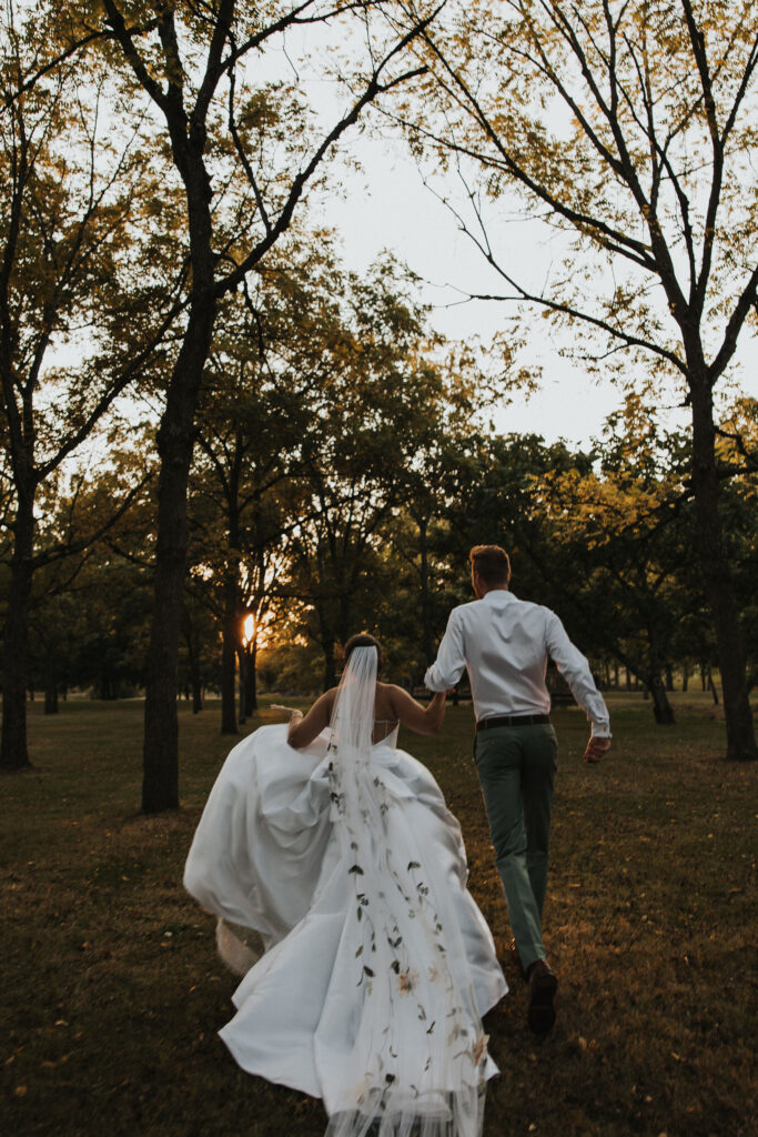 couple runs through woods at sunset outdoor wedding