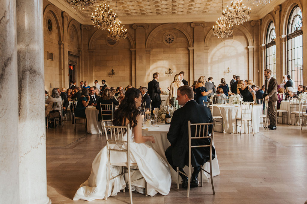 couple sits with guests during wedding reception