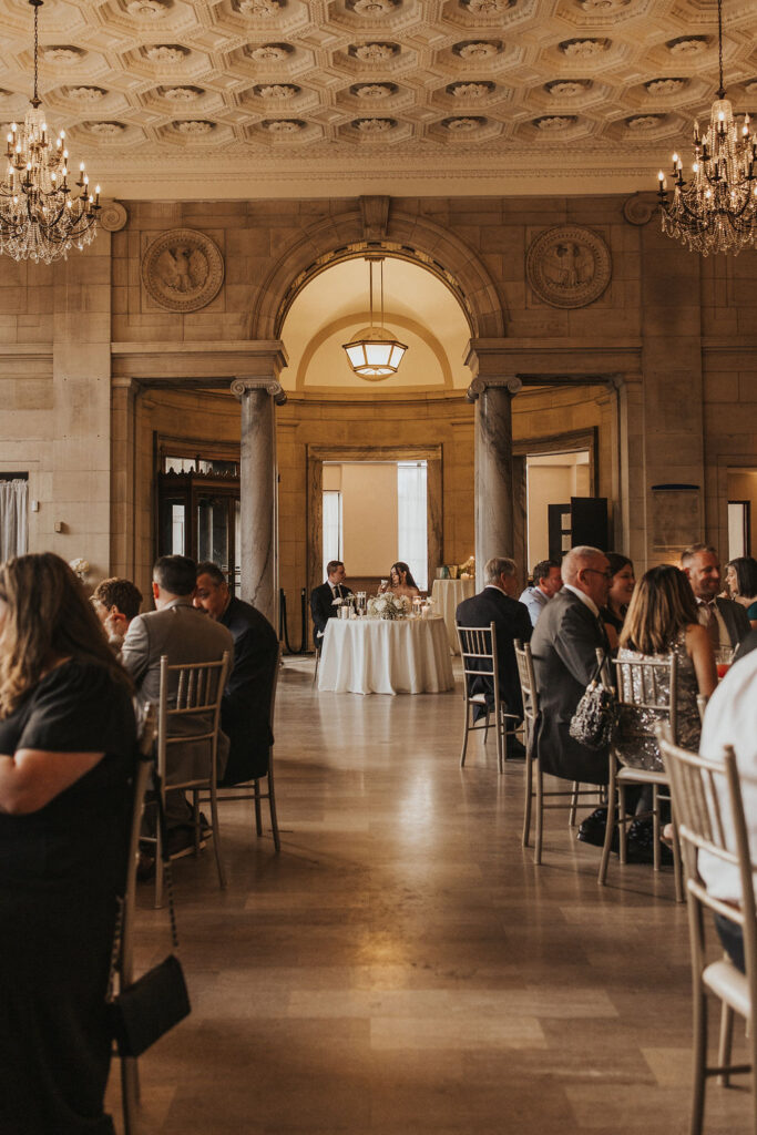 couple sits with guests during wedding reception 