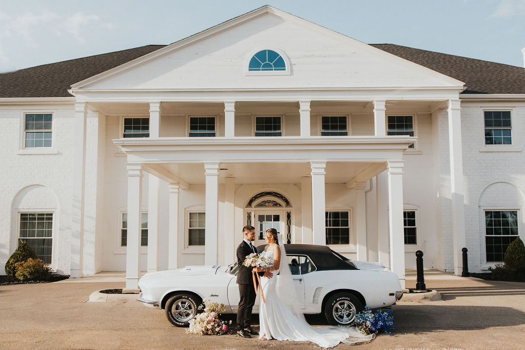 couple poses in front of car at historic home wedding venue