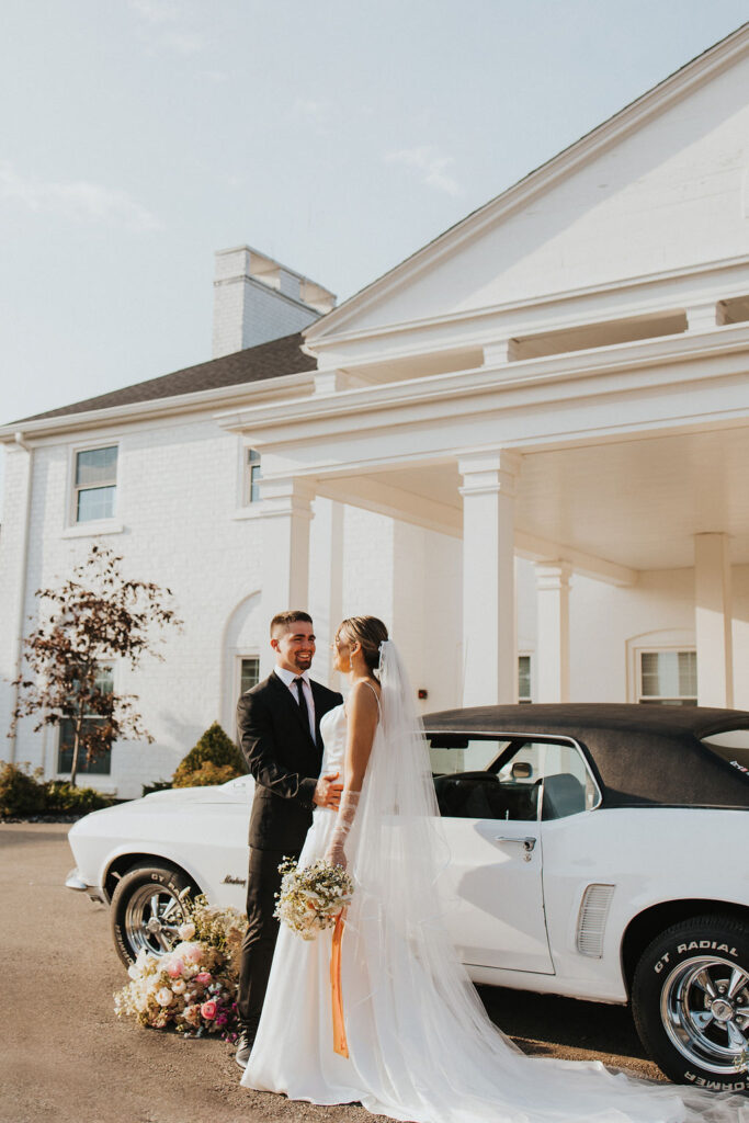 couple laughs together posing on white car