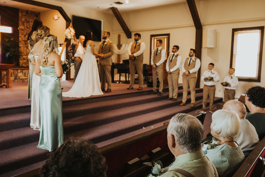 couple exchanges vows in church surrounded by wedding party