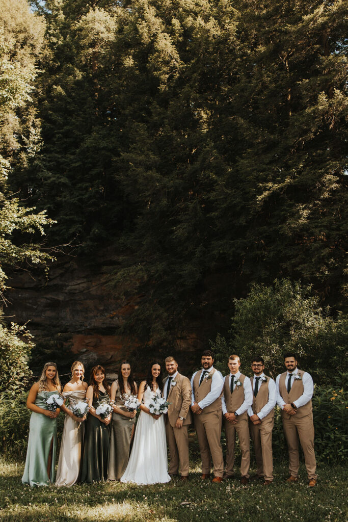 couple poses with wedding party in forest