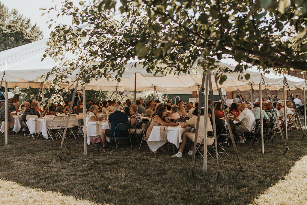 guests sit at tables under tent at backyard wedding reception 