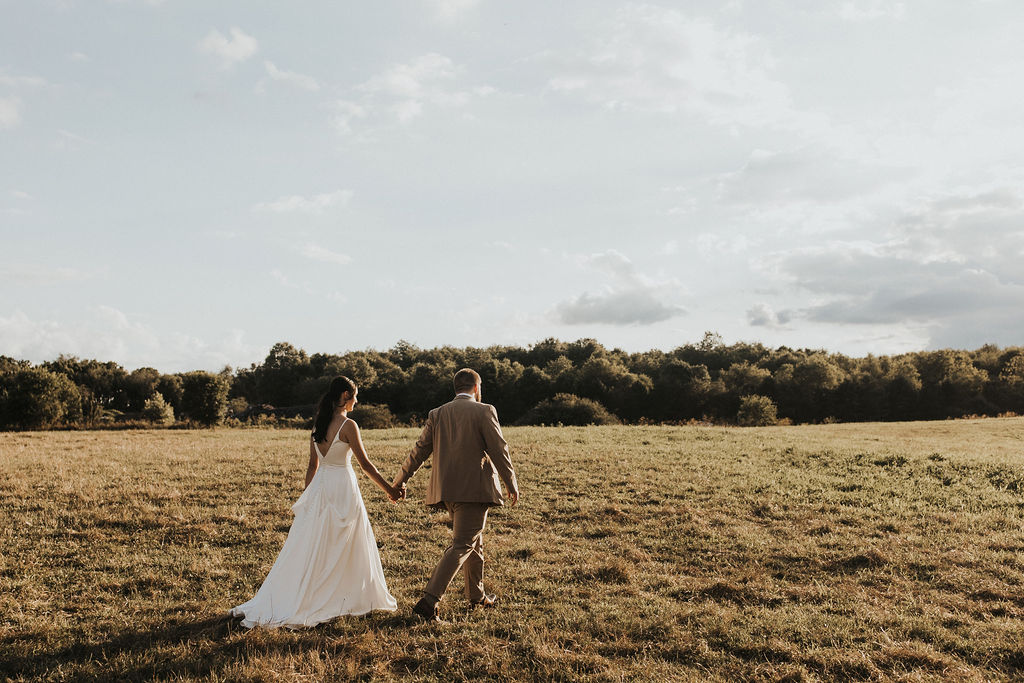 couple walks across field at backyard wedding reception