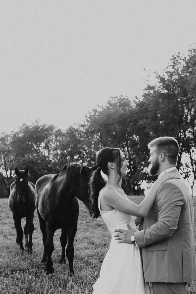 couple embraces in field with horses