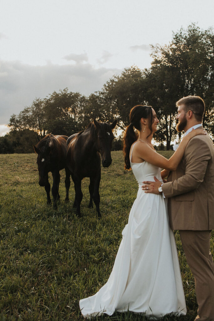 couple embraces in field with horses