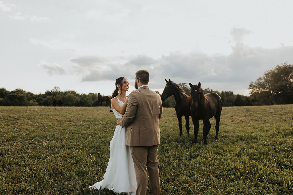 couple embraces in field with horses