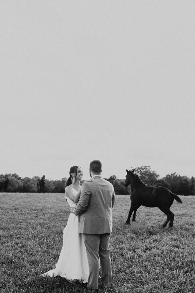 couple embraces in field with horses