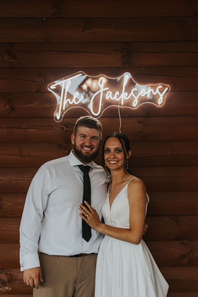 couple embraces under neon wedding name light