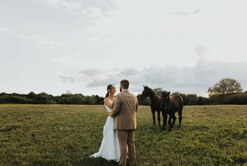 couple embraces with horses at farm