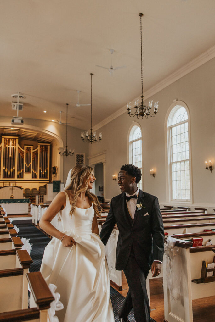 couple walks along church pews laughing 