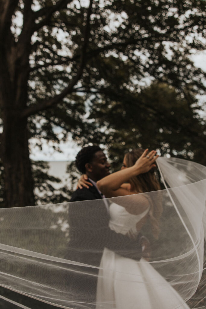 couple embraces with veil floating in the wind