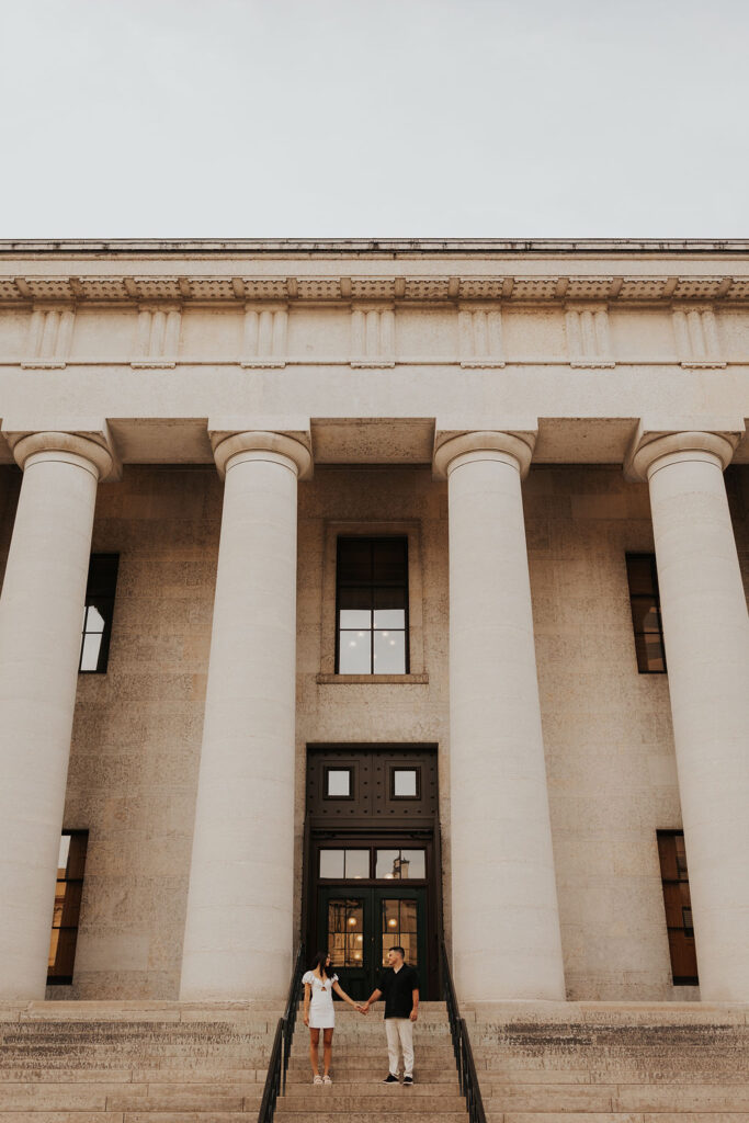 couple stands together holding hands on the steps in front of Ohio Statehouse