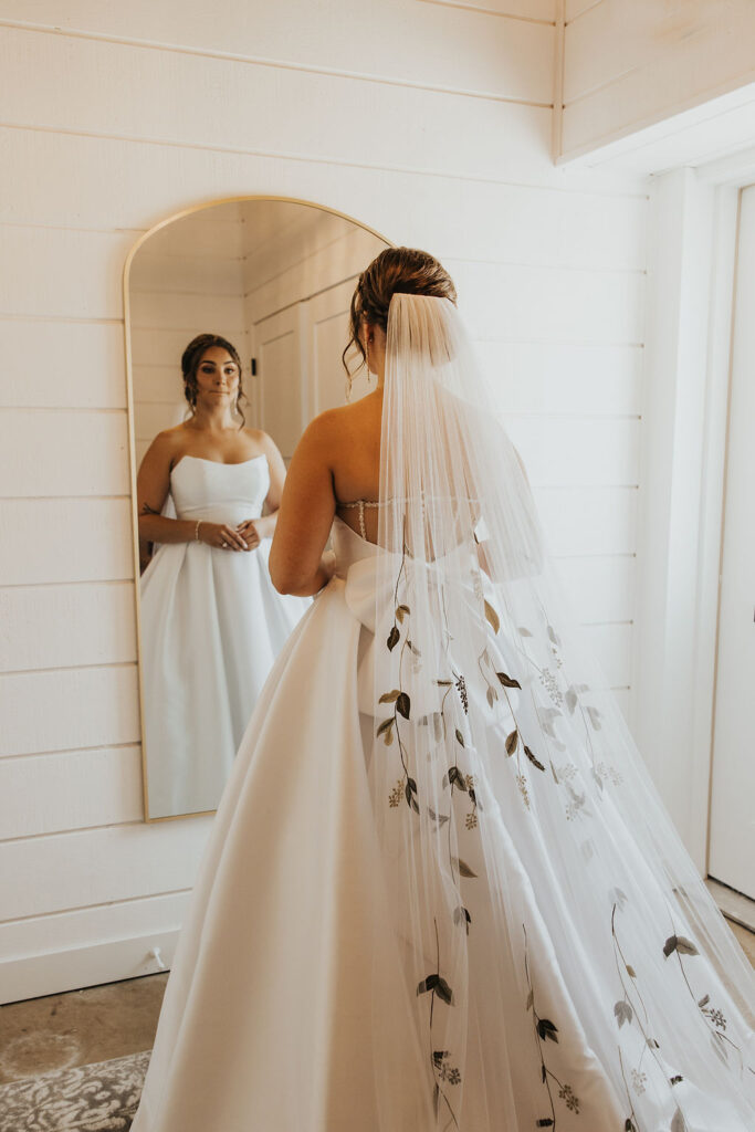 bride looking at herself in the mirror with wedding dress and veil on