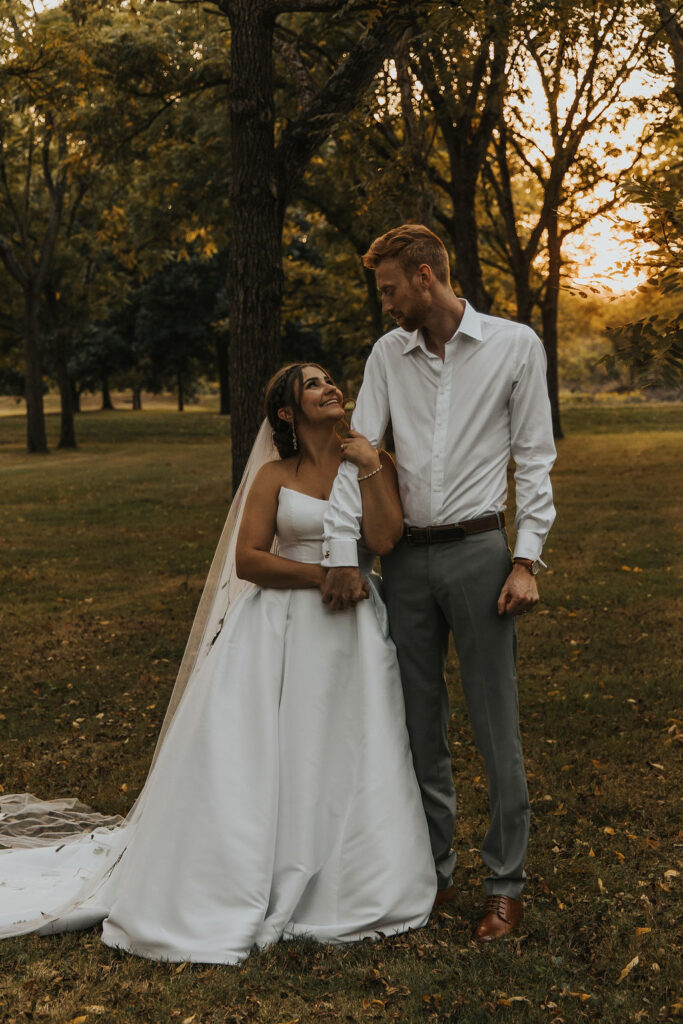 couple pose together among the trees at sunset