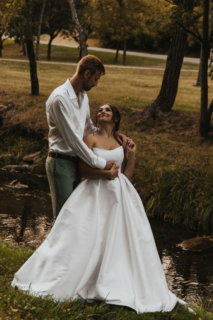 couple pose together among the trees and river at sunset