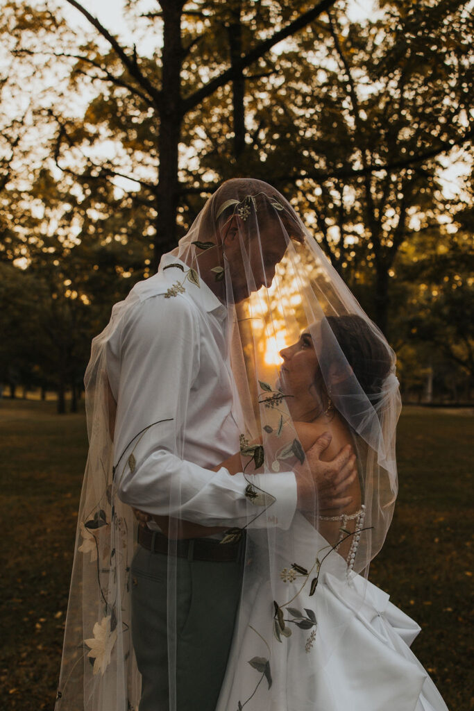 couple embrace with veil over them at sunset