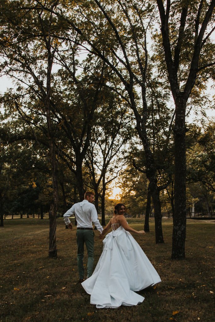 couple run together holding hands among the trees at sunset
