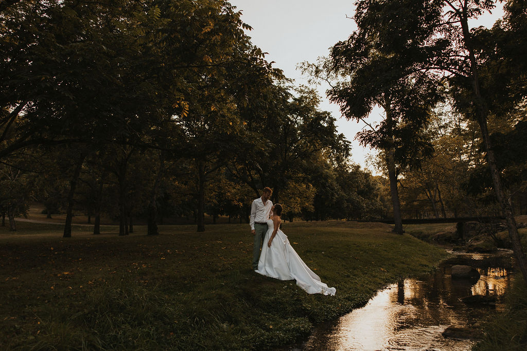 couple pose together among the trees and river at sunset