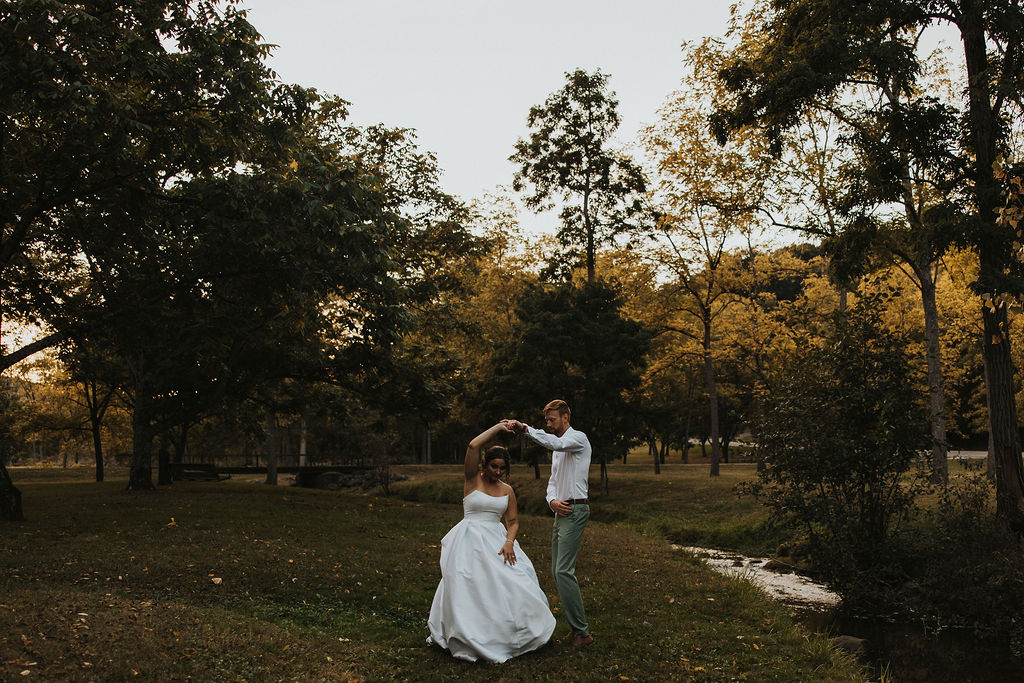 couple twirl together among the trees and river at sunset