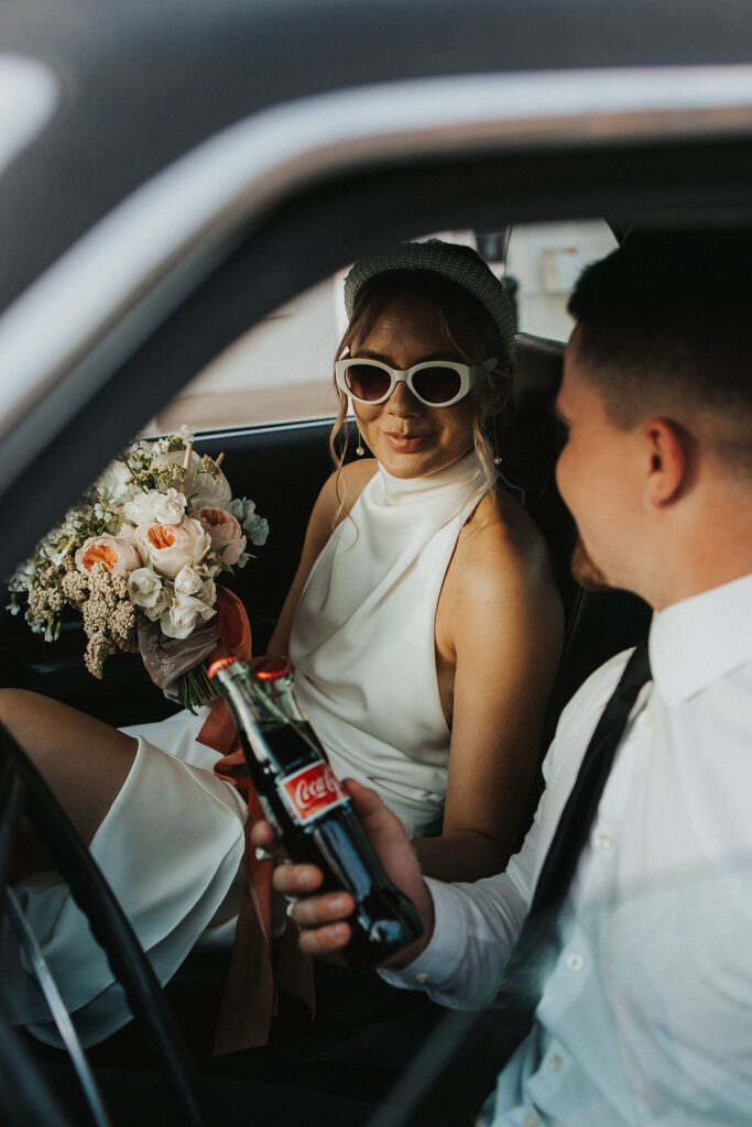 couple pose in classic car with a coke and flowers