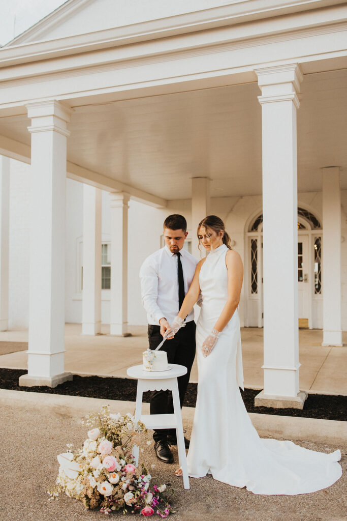 couple cuts cake in front of entrance of Westbrook Country club