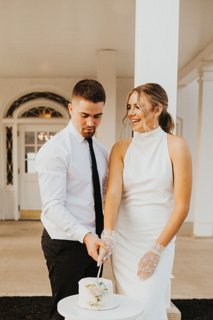 couple cuts cake in front of entrance of Westbrook Country club