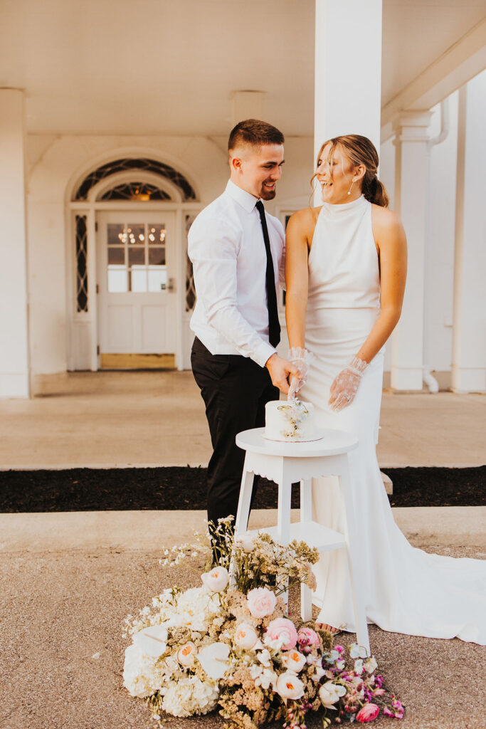 couple cuts cake in front of entrance of Westbrook Country club