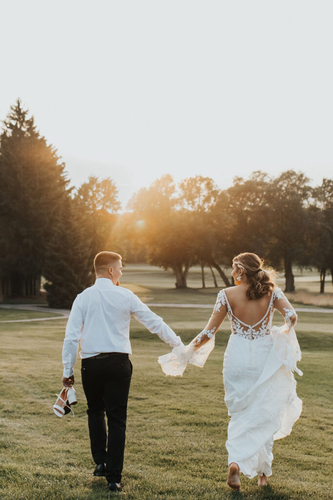 couple run together hand in hand on golf course greens during sunset
